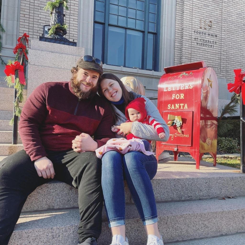 Image of Dex Fierro along with his wife and daughter sitting on some concrete steps in front of a "Letter for Santa" mailbox and some other Christmas-themed decorations.