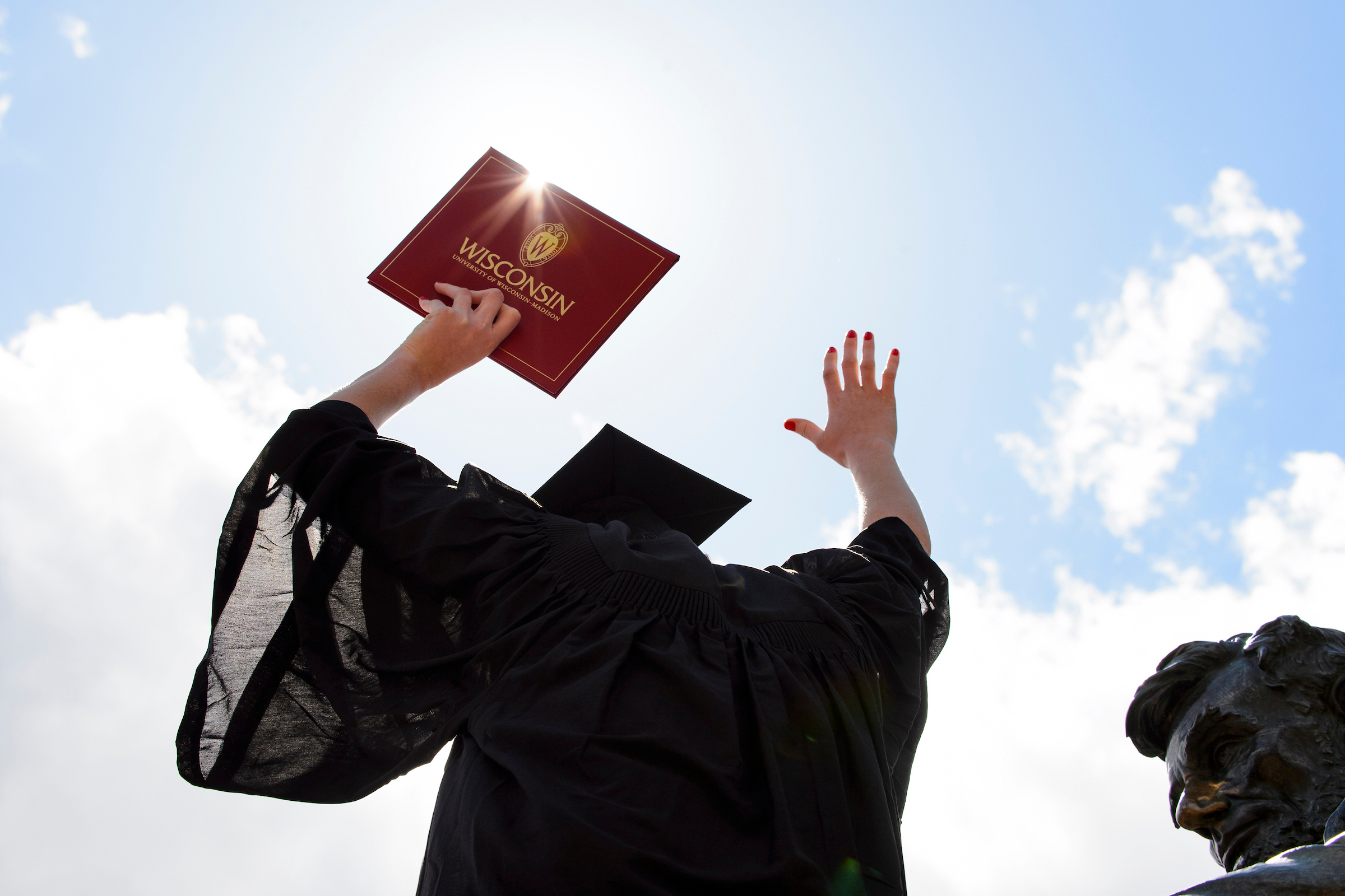 Student in a graduation gown with hands in the sky holding their diploma